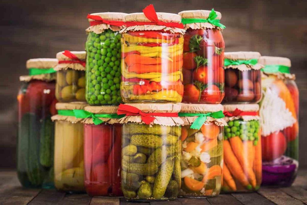 "Jars of homemade pickles with various vegetables and spices inside, placed on a wooden surface."